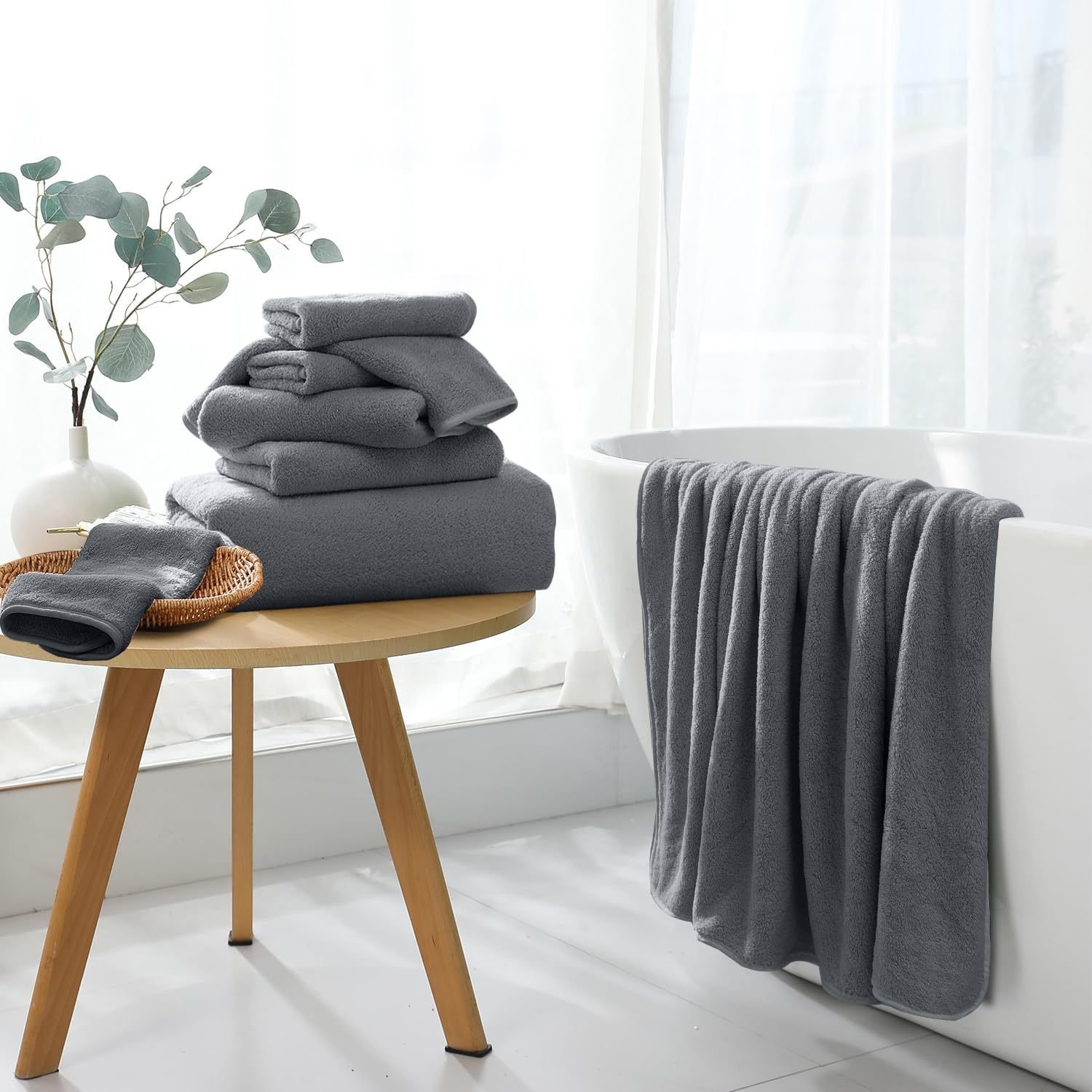 Grey coral fleece bath towels folded on a side table beside a bath